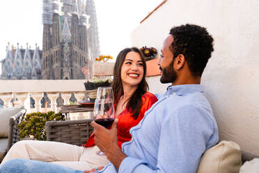 Multiracial beautiful happy couple of lovers dating on rooftop balcony at Sagrada Familia, Barcelona - Multiethnic people having romantic aperitif on a terrace with city view , concepts about tourism and people lifestyle - DMDF08194