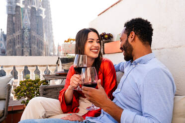 Multiracial beautiful happy couple of lovers dating on rooftop balcony at Sagrada Familia, Barcelona - Multiethnic people having romantic aperitif on a terrace with city view , concepts about tourism and people lifestyle - DMDF08199