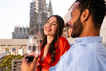 Multiracial beautiful happy couple of lovers dating on rooftop balcony at Sagrada Familia, Barcelona - Multiethnic people having romantic aperitif on a terrace with city view , concepts about tourism and people lifestyle - DMDF08200