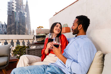 Multiracial beautiful happy couple of lovers dating on rooftop balcony at Sagrada Familia, Barcelona - Multiethnic people having romantic aperitif on a terrace with city view , concepts about tourism and people lifestyle - DMDF08201