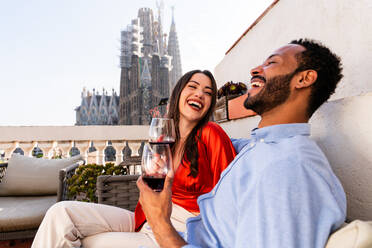 Multiracial beautiful happy couple of lovers dating on rooftop balcony at Sagrada Familia, Barcelona - Multiethnic people having romantic aperitif on a terrace with city view , concepts about tourism and people lifestyle - DMDF08203