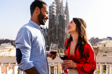 Multirassisches glückliches Liebespaar auf einem Dachbalkon an der Sagrada Familia, Barcelona - Multiethnische Menschen bei einem romantischen Aperitif auf einer Terrasse mit Blick auf die Stadt, Konzepte über Tourismus und Lebensstil der Menschen - DMDF08208