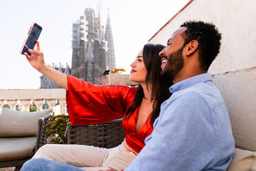 Multirassisches glückliches Liebespaar auf einem Dachbalkon an der Sagrada Familia, Barcelona - Multiethnische Menschen bei einem romantischen Treffen auf einer Terrasse mit Blick auf die Stadt, Konzepte für Tourismus und Lebensstil der Menschen - DMDF08216