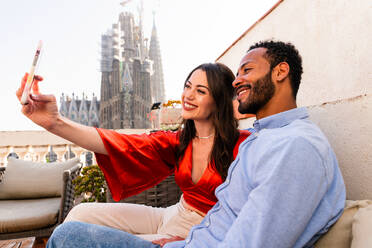 Multirassisches glückliches Liebespaar auf einem Dachbalkon an der Sagrada Familia, Barcelona - Multiethnische Menschen bei einem romantischen Treffen auf einer Terrasse mit Blick auf die Stadt, Konzepte für Tourismus und Lebensstil der Menschen - DMDF08217