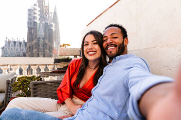 Multiracial beautiful happy couple of lovers dating on rooftop balcony at Sagrada Familia, Barcelona - Multiethnic people having romantic meeting on a terrace with city view , concepts about tourism and people lifestyle - DMDF08218