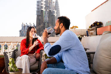 Multiracial beautiful happy couple of lovers dating on rooftop balcony at Sagrada Familia, Barcelona - Multiethnic people having romantic aperitif on a terrace with city view , concepts about tourism and people lifestyle - DMDF08224