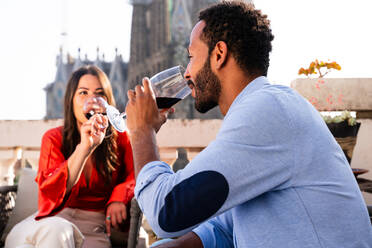 Multiracial beautiful happy couple of lovers dating on rooftop balcony at Sagrada Familia, Barcelona - Multiethnic people having romantic aperitif on a terrace with city view , concepts about tourism and people lifestyle - DMDF08227