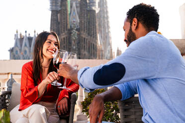 Multiracial beautiful happy couple of lovers dating on rooftop balcony at Sagrada Familia, Barcelona - Multiethnic people having romantic aperitif on a terrace with city view , concepts about tourism and people lifestyle - DMDF08228