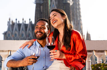 Multiracial beautiful happy couple of lovers dating on rooftop balcony at Sagrada Familia, Barcelona - Multiethnic people having romantic aperitif on a terrace with city view , concepts about tourism and people lifestyle - DMDF08235