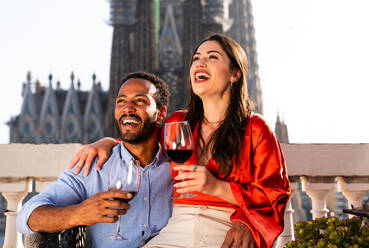 Multiracial beautiful happy couple of lovers dating on rooftop balcony at Sagrada Familia, Barcelona - Multiethnic people having romantic aperitif on a terrace with city view , concepts about tourism and people lifestyle - DMDF08237