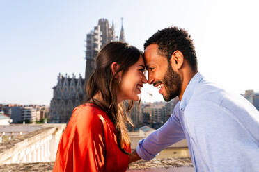 Multiracial beautiful happy couple of lovers dating on rooftop balcony at Sagrada Familia, Barcelona - Multiethnic people having romantic meeting on a terrace with city view , concepts about tourism and people lifestyle - DMDF08246