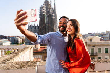 Multirassisches glückliches Liebespaar auf einem Dachbalkon an der Sagrada Familia, Barcelona - Multiethnische Menschen bei einem romantischen Treffen auf einer Terrasse mit Blick auf die Stadt, Konzepte für Tourismus und Lebensstil der Menschen - DMDF08258