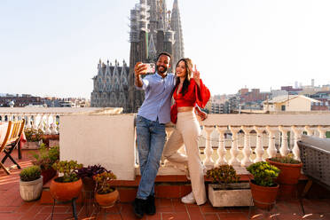 Multirassisches glückliches Liebespaar auf einem Dachbalkon an der Sagrada Familia, Barcelona - Multiethnische Menschen bei einem romantischen Treffen auf einer Terrasse mit Blick auf die Stadt, Konzepte für Tourismus und Lebensstil der Menschen - DMDF08265