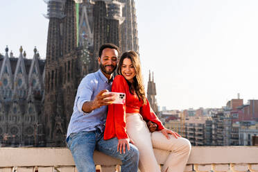 Multirassisches glückliches Liebespaar auf einem Dachbalkon an der Sagrada Familia, Barcelona - Multiethnische Menschen bei einem romantischen Treffen auf einer Terrasse mit Blick auf die Stadt, Konzepte für Tourismus und Lebensstil der Menschen - DMDF08276
