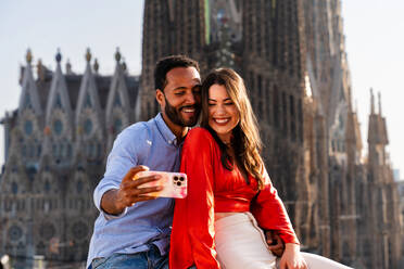 Multirassisches glückliches Liebespaar auf einem Dachbalkon an der Sagrada Familia, Barcelona - Multiethnische Menschen bei einem romantischen Treffen auf einer Terrasse mit Blick auf die Stadt, Konzepte für Tourismus und Lebensstil der Menschen - DMDF08277