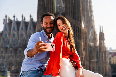 Multirassisches glückliches Liebespaar auf einem Dachbalkon an der Sagrada Familia, Barcelona - Multiethnische Menschen bei einem romantischen Treffen auf einer Terrasse mit Blick auf die Stadt, Konzepte für Tourismus und Lebensstil der Menschen - DMDF08279