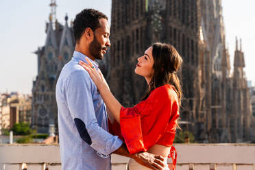 Multiracial beautiful happy couple of lovers dating on rooftop balcony at Sagrada Familia, Barcelona - Multiethnic people having romantic meeting on a terrace with city view , concepts about tourism and people lifestyle - DMDF08290