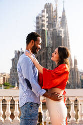 Multiracial beautiful happy couple of lovers dating on rooftop balcony at Sagrada Familia, Barcelona - Multiethnic people having romantic meeting on a terrace with city view , concepts about tourism and people lifestyle - DMDF08292