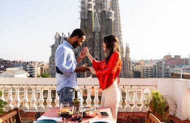 Multirassisches glückliches Liebespaar auf einem Dachbalkon an der Sagrada Familia, Barcelona - Multiethnische Menschen beim romantischen Aperitif-Dinner auf einer Terrasse mit Blick auf die Stadt, Konzepte über Tourismus und Lebensstil der Menschen - DMDF08294