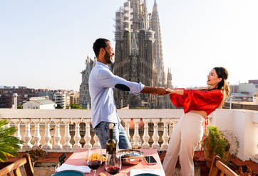 Multirassisches glückliches Liebespaar auf einem Dachbalkon an der Sagrada Familia, Barcelona - Multiethnische Menschen beim romantischen Aperitif-Dinner auf einer Terrasse mit Blick auf die Stadt, Konzepte über Tourismus und Lebensstil der Menschen - DMDF08297