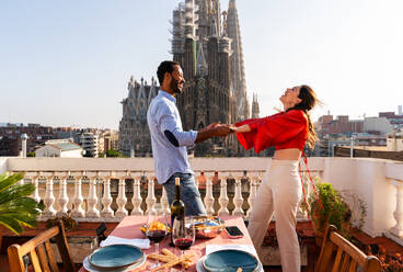 Multirassisches glückliches Liebespaar auf einem Dachbalkon an der Sagrada Familia, Barcelona - Multiethnische Menschen beim romantischen Aperitif-Dinner auf einer Terrasse mit Blick auf die Stadt, Konzepte über Tourismus und Lebensstil der Menschen - DMDF08299