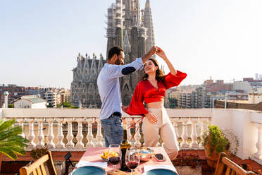 Multirassisches glückliches Liebespaar auf einem Dachbalkon an der Sagrada Familia, Barcelona - Multiethnische Menschen beim romantischen Aperitif-Dinner auf einer Terrasse mit Blick auf die Stadt, Konzepte über Tourismus und Lebensstil der Menschen - DMDF08301
