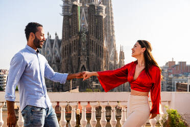 Multirassisches glückliches Liebespaar auf einem Dachbalkon an der Sagrada Familia, Barcelona - Multiethnische Menschen beim romantischen Aperitif-Dinner auf einer Terrasse mit Blick auf die Stadt, Konzepte über Tourismus und Lebensstil der Menschen - DMDF08302