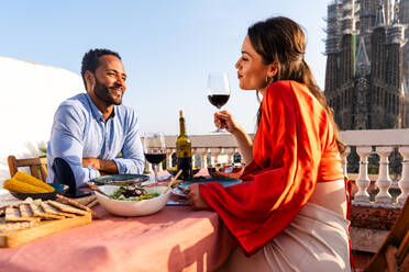 Multirassisches glückliches Liebespaar auf einem Dachbalkon an der Sagrada Familia, Barcelona - Multiethnische Menschen beim romantischen Aperitif-Dinner auf einer Terrasse mit Blick auf die Stadt, Konzepte über Tourismus und Lebensstil der Menschen - DMDF08319