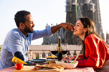 Multirassisches glückliches Liebespaar auf einem Dachbalkon an der Sagrada Familia, Barcelona - Multiethnische Menschen beim romantischen Aperitif-Dinner auf einer Terrasse mit Blick auf die Stadt, Konzepte über Tourismus und Lebensstil der Menschen - DMDF08320