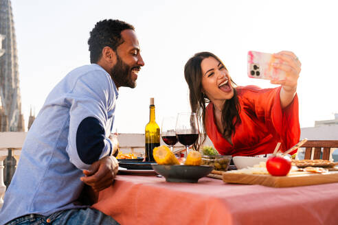 Multirassisches glückliches Liebespaar auf einem Dachbalkon an der Sagrada Familia, Barcelona - Multiethnische Menschen beim romantischen Aperitif-Dinner auf einer Terrasse mit Blick auf die Stadt, Konzepte über Tourismus und Lebensstil der Menschen - DMDF08330