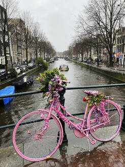 Rosa Fahrrad in der Nähe des Geländers an der Gracht in Amsterdam in den Niederlanden - PBTF00393