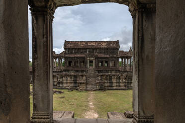 A serene view of Angkor Wat, framed by a weathered stone doorway, reveals the grandeur of Cambodia's iconic temple complex against a cloudy sky. - ADSF50816
