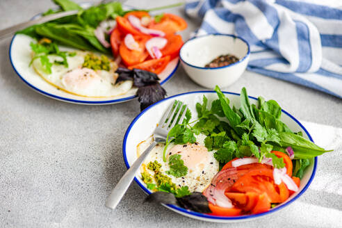 Eine nahrhafte Keto-Mahlzeit, bestehend aus Blattgemüse, Avocado, Eiern und Tomaten, serviert auf einem weißen Teller mit blauem Rand. - ADSF50822