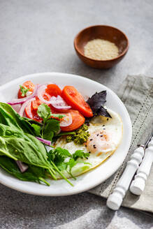 Frisches Keto-Frühstück mit pochierten Eiern, Spinat, Tomaten und Kräutern auf einem weißen Teller, ideal für eine kohlenhydratarme Ernährung. - ADSF50824