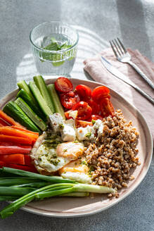 A nutritious breakfast concept showcasing a balanced meal with fresh vegetables, creamy feta, protein-rich buckwheat, and pesto-topped fried eggs. - ADSF50827