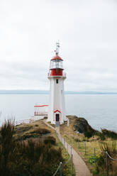 Ein ruhiger Blick auf den traditionellen weiß-roten Leuchtturm von Sheringham Point auf Vancouver Island mit Blick auf das ruhige Wasser des Pazifischen Ozeans unter einem bewölkten Himmel. - ADSF50841