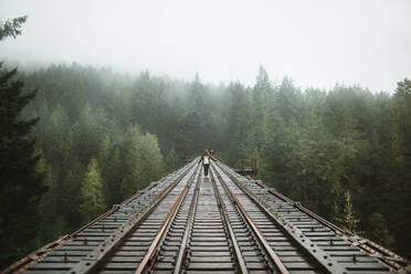 Eine Frau steht mitten auf alten Eisenbahnschienen, umhüllt von einem dichten, nebligen Wald auf Vancouver Island. - ADSF50845