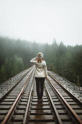 Eine Frau in warmer Kleidung betrachtet eine neblige Landschaft, während sie in den Wäldern von Vancouver Island entlang einer Eisenbahnlinie spaziert. - ADSF50848