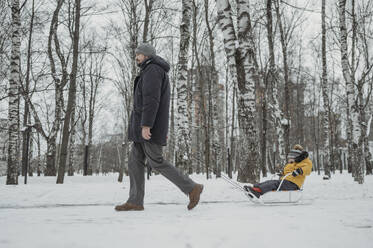 Vater schlittelt mit seinem Sohn durch den Schnee im Winterpark - ANAF02607