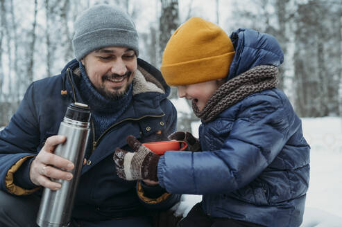 Smiling father and son having tea in winter - ANAF02617