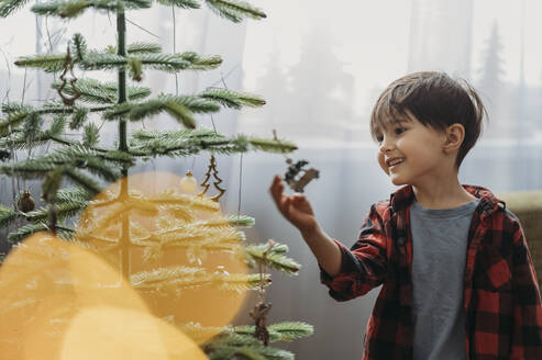 Lächelnder Junge beim Schmücken des Weihnachtsbaums zu Hause - ANAF02623