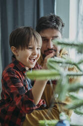 Glücklicher Vater und Sohn schmücken den Weihnachtsbaum zu Hause - ANAF02626