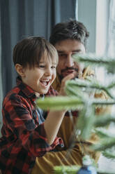 Happy father and son decorating Christmas tree at home - ANAF02626