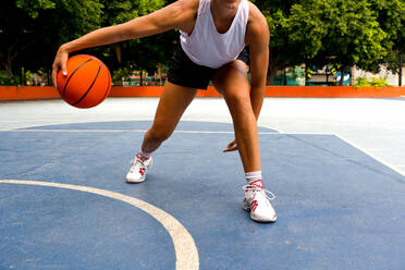 Crop unrecognizable sporty female in activewear dribbling while playing basketball on court during sunny summer day - ADSF50929