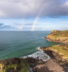 Aerial view of swimmer at secret cove with a rainbow in the sea, Talland Bay, Cornwall, United Kingdom. - AAEF24704