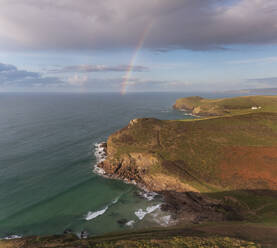 Aerial view of swimmer at secret cove with a rainbow in the sea, Talland Bay, Cornwall, United Kingdom. - AAEF24705