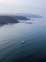 Aerial view of a boat crossing the lake at sunset with mountain in background in Malshej ghat, Maharashtra, India. - AAEF24713