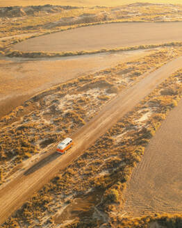 Luftaufnahme eines orangefarbenen Oldtimer-Wohnmobils in der Wüste Bardenas Reales bei Sonnenaufgang, Navarra, Spanien. - AAEF24824