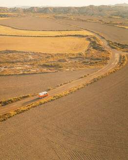 Luftaufnahme eines orangefarbenen Oldtimer-Wohnmobils in der Wüste Bardenas Reales bei Sonnenaufgang, Navarra, Spanien. - AAEF24826