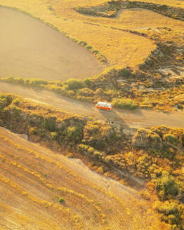 Luftaufnahme eines orangefarbenen Oldtimer-Wohnmobils in der Wüste Bardenas Reales bei Sonnenaufgang, Navarra, Spanien. - AAEF24827